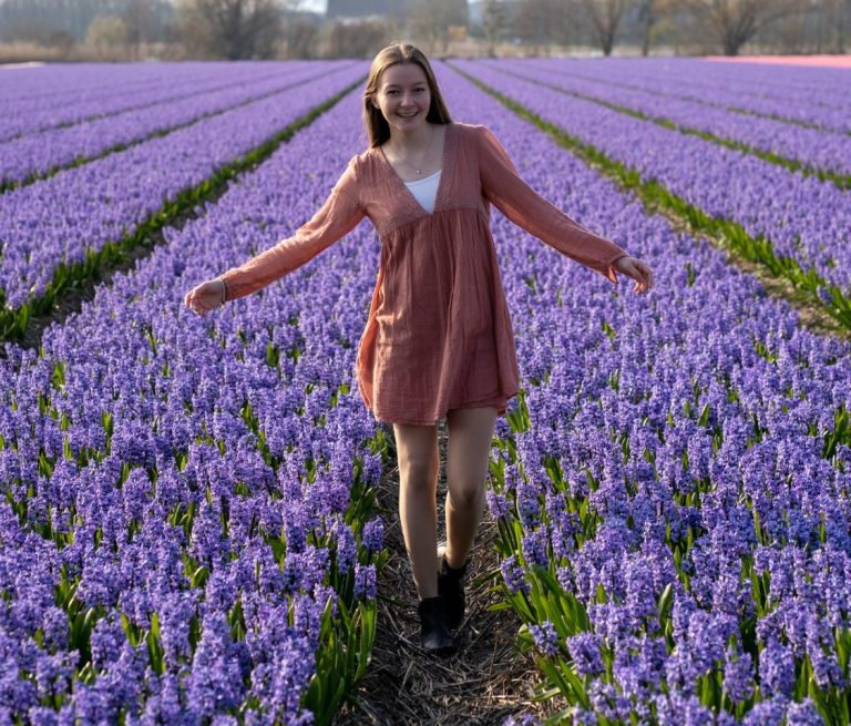 Junge Frau läuft glücklich durch einen Tulpenfeld mit lila Tulpen. die Frau hat ein Kleid an